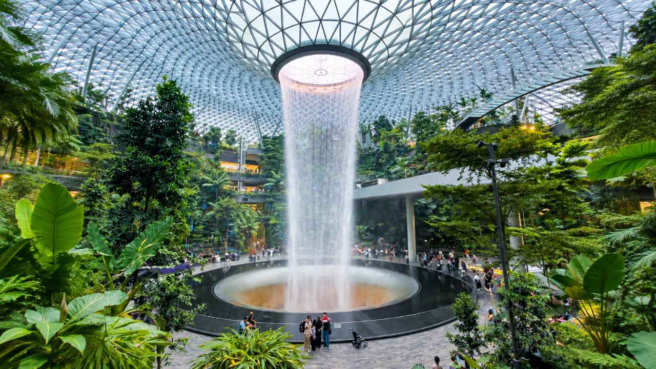 Air terjun HSBC Rain Vortex di Jewel Changi Airport jatuh dari puncak kubah kaca dan dikelilingi Shiseido Forest Valley yang hijau