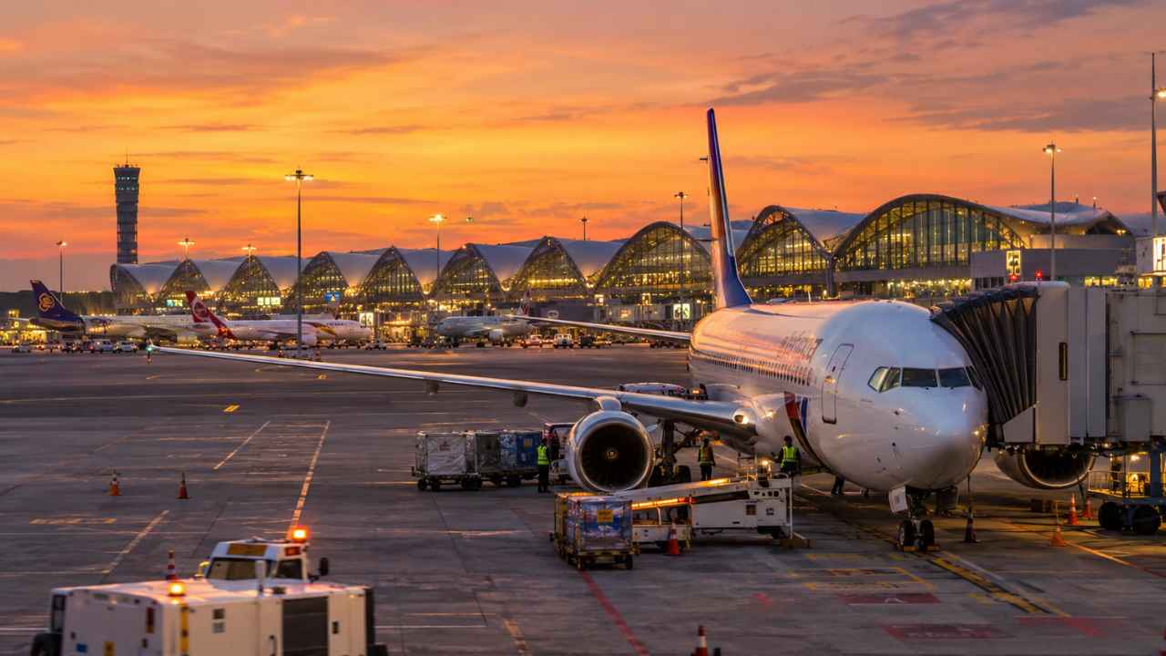 Pesawat komersial di apron Bandara Soekarno-Hatta dengan jadwal penerbangan Jakarta ke Bangkok di latar belakang