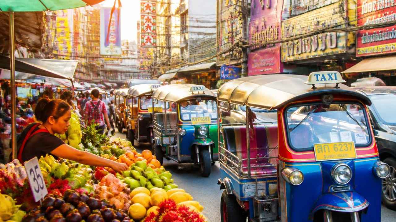 Tuk-tuk berwarna cerah melintas di jalanan Bangkok dengan deretan gedung kota di latar belakang
