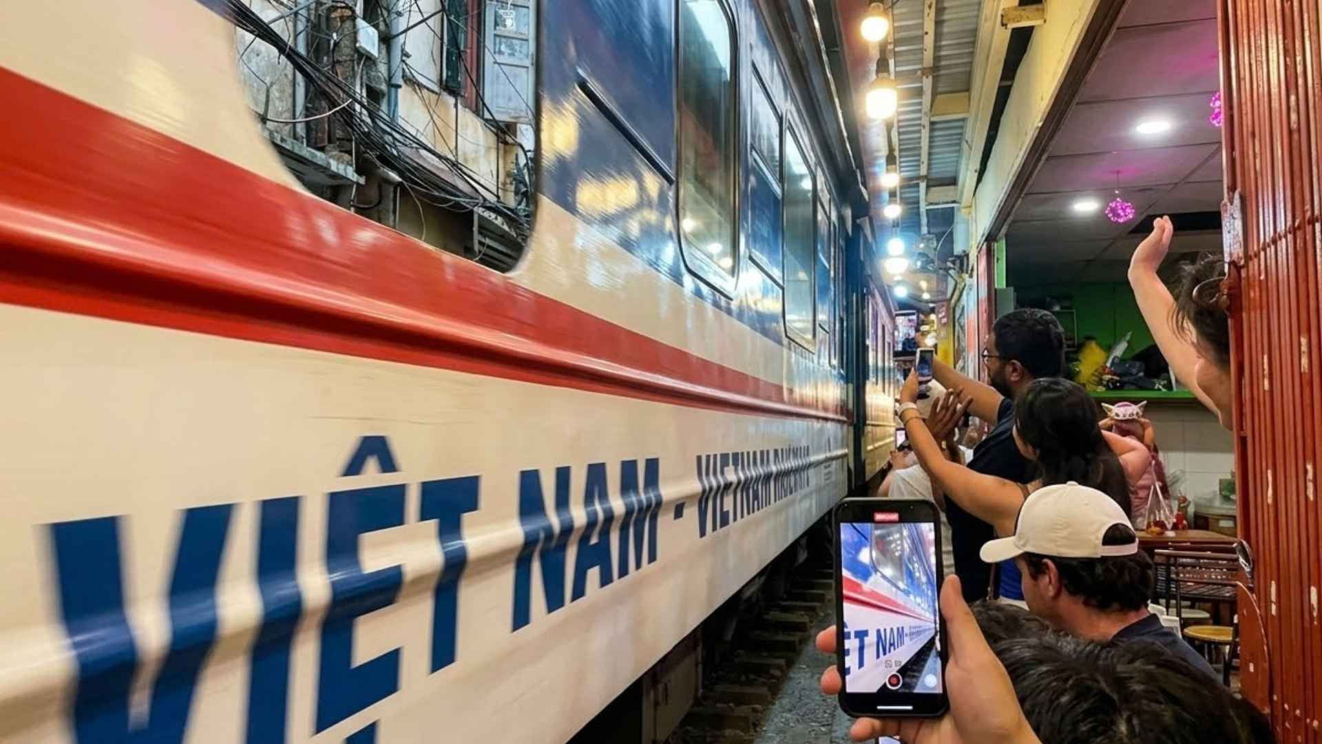 Kereta Vietnam Railways melintas sangat dekat di lorong Train Street sementara wisatawan mengangkat ponsel merekam dari kedua sisi rel